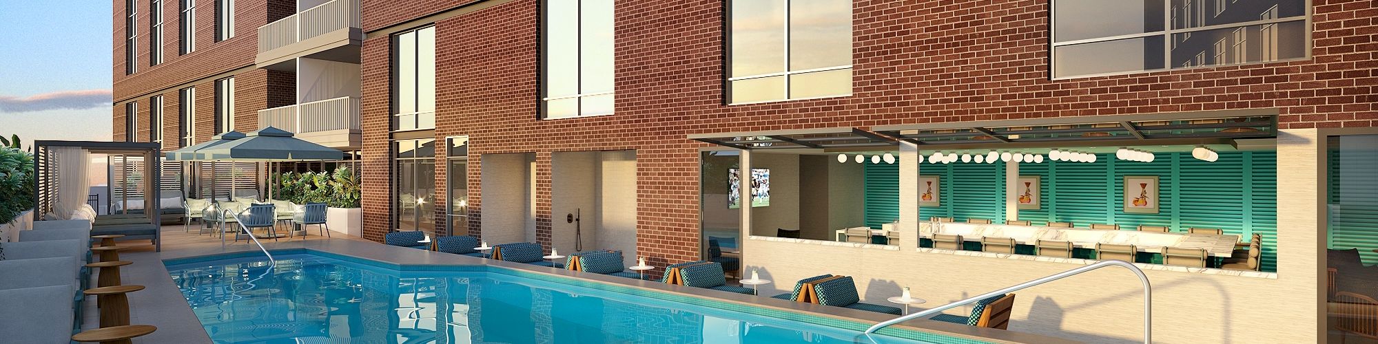 A modern brick apartment complex with a long rectangular outdoor pool, lounge chairs, umbrellas, and a glass-walled indoor area, under a clear sky.