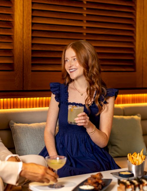 A man and woman sit in a restaurant booth, smiling as they chat over drinks and food.