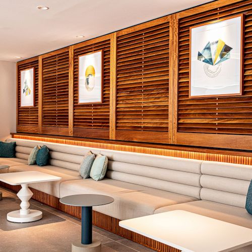 Modern lounge with a wood slat accent wall, framed artwork, and a long beige sofa under warm strip lighting.