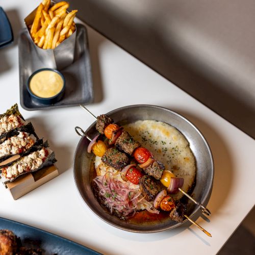 A top-down view of a candlelit breakfast or brunch spread with a skillet of eggs and toppings, sliced bread, and small bowls.