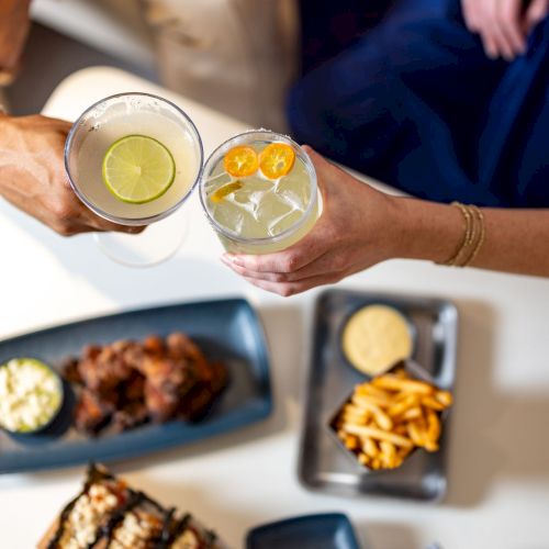A spread of bite-sized treats: eggs benedict, roasted meat, grilled skewers, pancakes or pastries, a dip, and a few rolled items, all on a table.