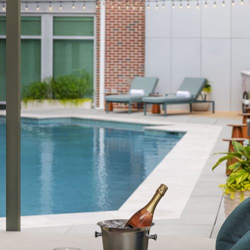 Outdoor poolside patio with lounge chairs, a brick-and-white building, and a chilled champagne bottle in an ice bucket.